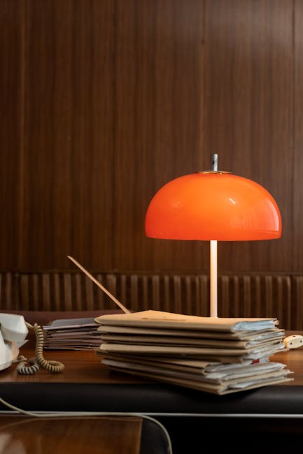 Retro office setting with a red lamp and stacked folders on a wooden desk, capturing a vintage vibe.